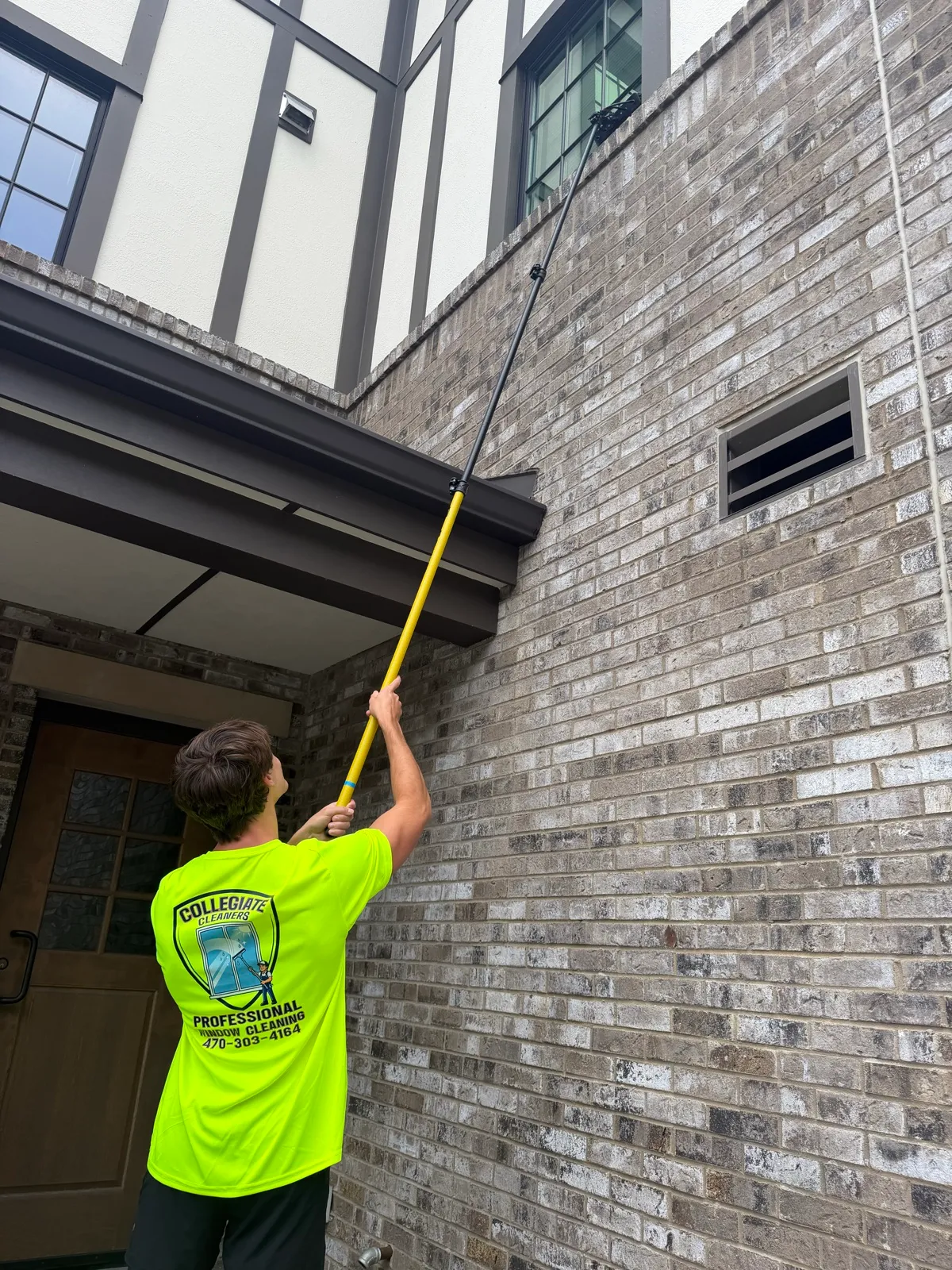 A Collegiate Cleaners team member in a branded shirt reaching a high window